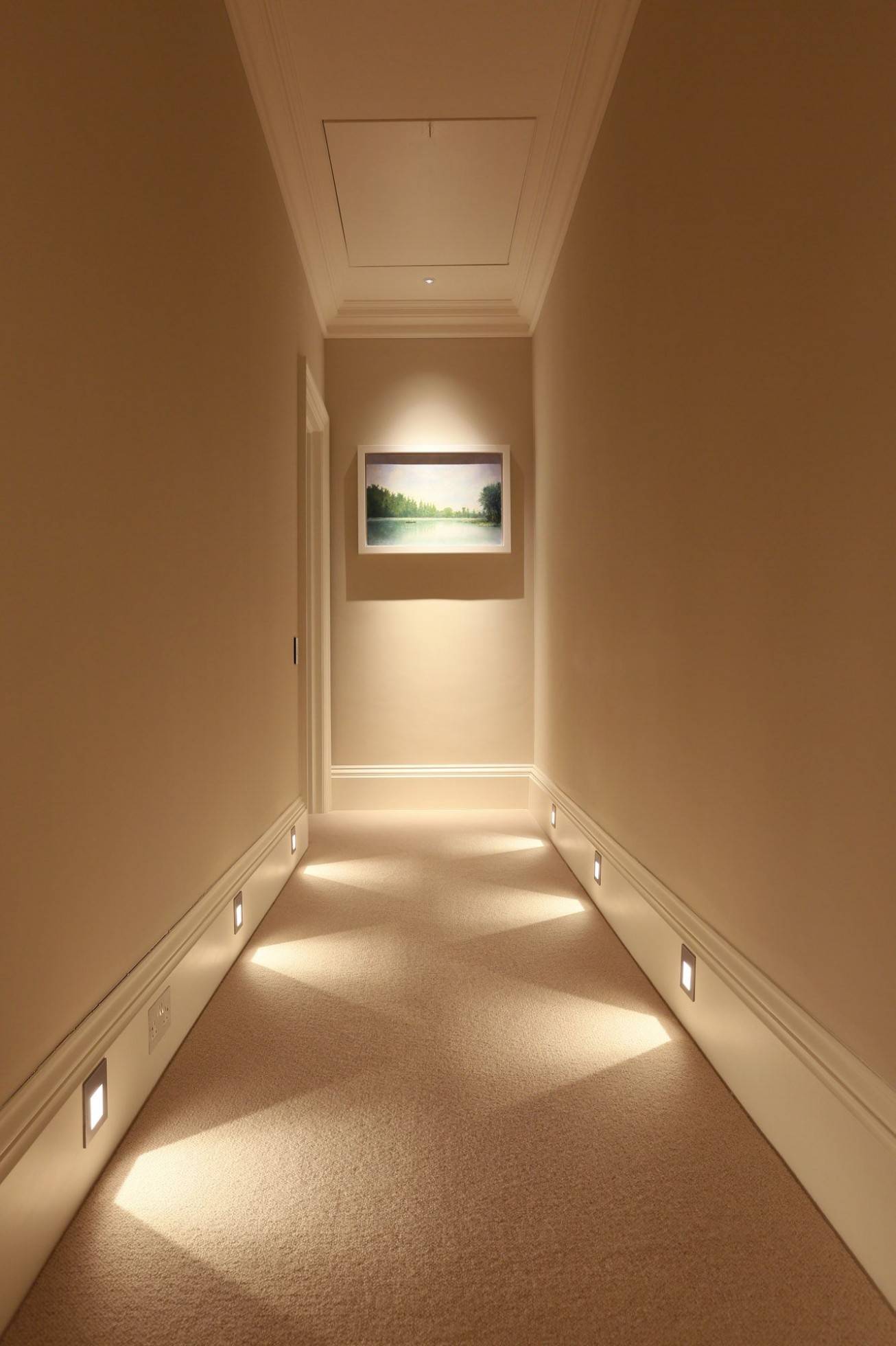 Pasillo moderno con rodapié blanco de PVC alto, luces empotradas y pared beige.