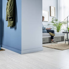 Rodapié canto recto pintable en sala moderna con pared azul y suelo de madera clara