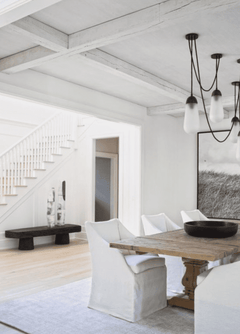 Salón moderno con vigas blancas decorativas en techo, mesa de madera y sillas blancas.