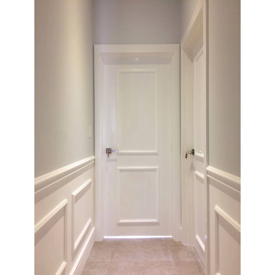 Pasillo interior con molduras decorativas blancas en paredes y puertas, suelo beige.