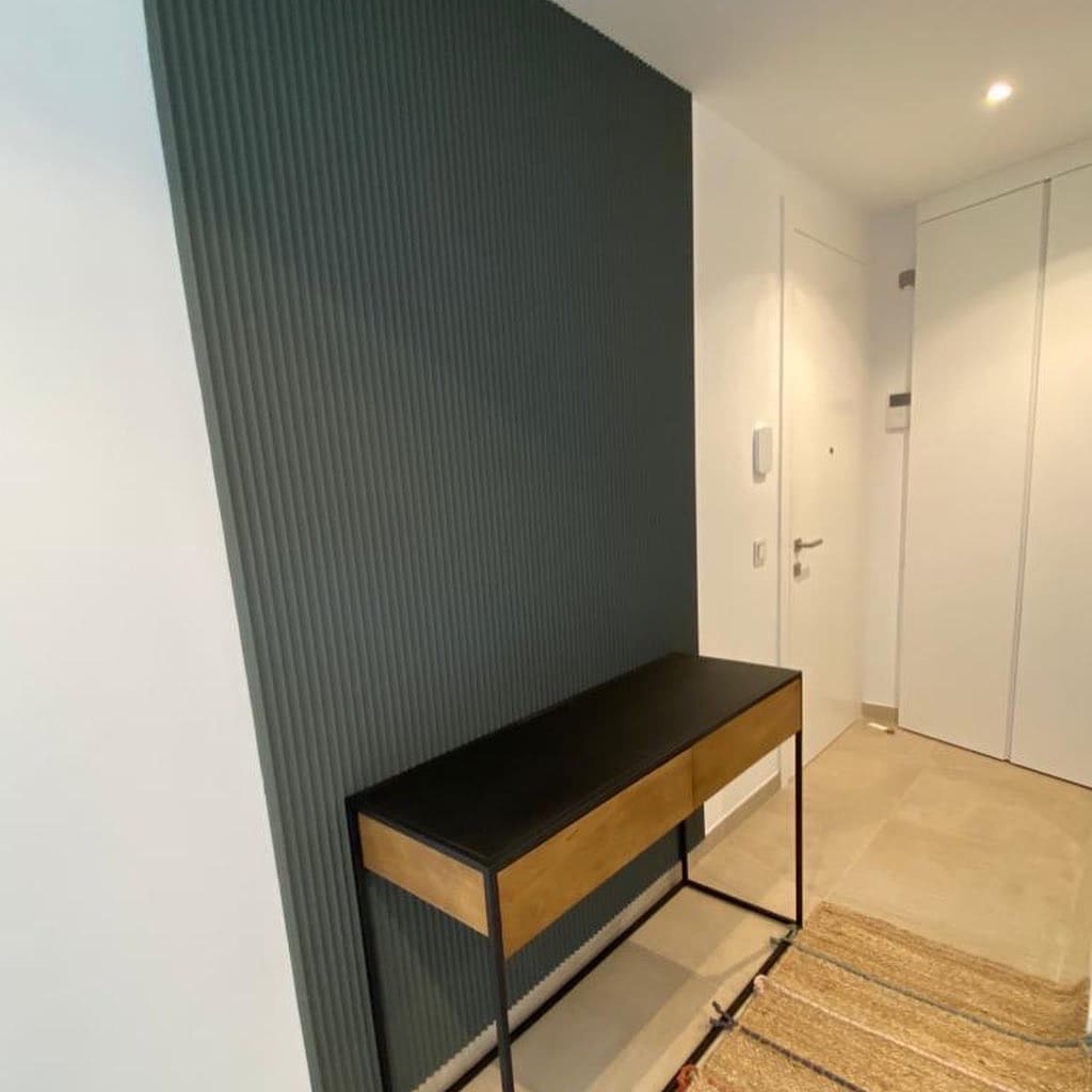 Pared decorativa con moldura verde, consola moderna y suelo claro en recibidor elegante.