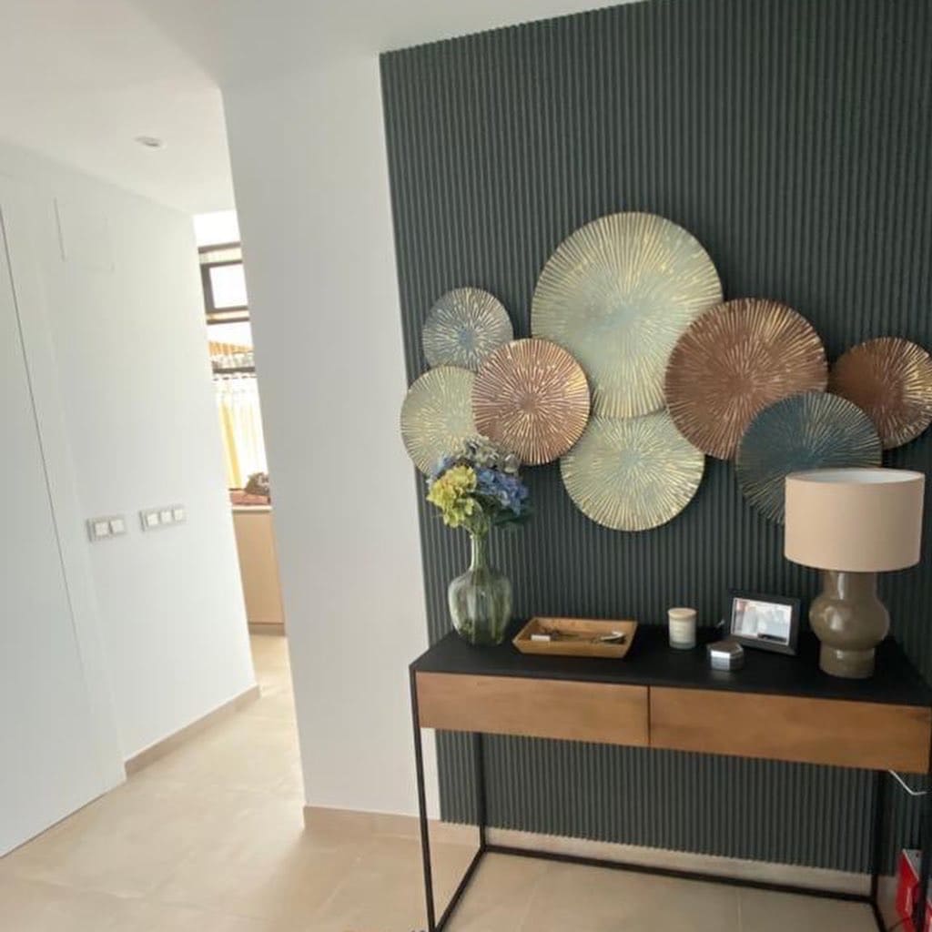 Panel decorativo verde oscuro con molduras verticales, mesa recibidor y arte de pared metálico.