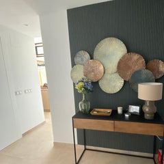 Panel decorativo verde oscuro con molduras verticales, mesa recibidor y arte de pared metálico.